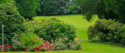 Lush flowerbeds in the summer garden. Evening time. Wide photo.