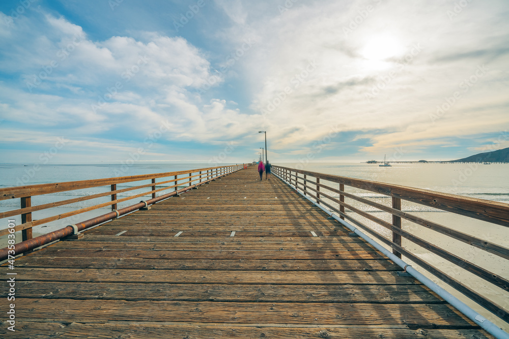 Wide long wooden pier on the beach with beautiful cloudy sky on background, California