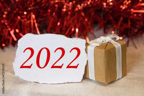 A white sheet of paper and a New Year's gift next to it on a red background. Space for text 2022. The concept of holidays. Christmas