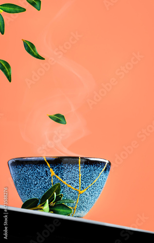 Bowl of green tea and levitation of tea leaves against a background of burnt sienna. Selective focus on cup. Steam rises above the bowl. Reclaimed ceramic blue cup, second life of things, recycling