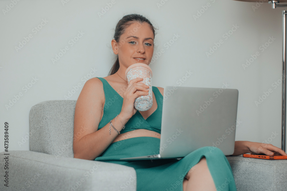 Mujer empresaria desayunando café mientras está sentada en el sillón de la habitación revisando los datos de su negocio online en su laptop Mujer empresaria desayunando café mientras está sentada en el sillón de la habitación revisando los datos de su negocio online en su laptop