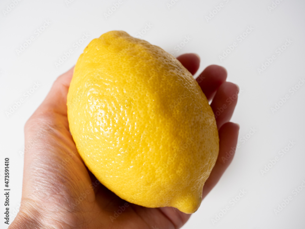 Close-up of a hand holding a yellow lemon. White background, side view Close-up of a hand holding a yellow lemon. White background, side view