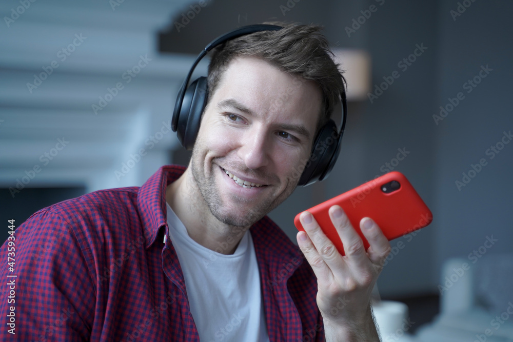 Smiling young German man in headphones recording voice message for collegue, using speakerphone Smiling young German man in headphones recording voice message for collegue, using speakerphone