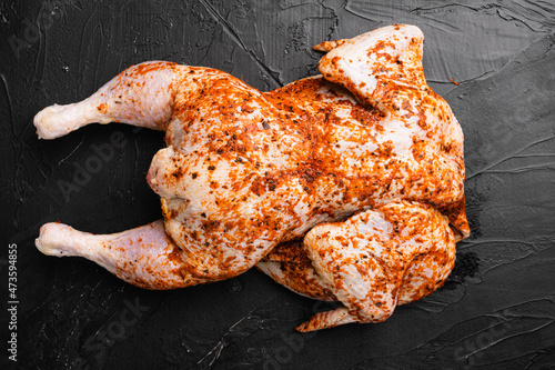 Raw chicken tabaka ready for cooking with ingredients, on black dark stone table background, top view flat lay