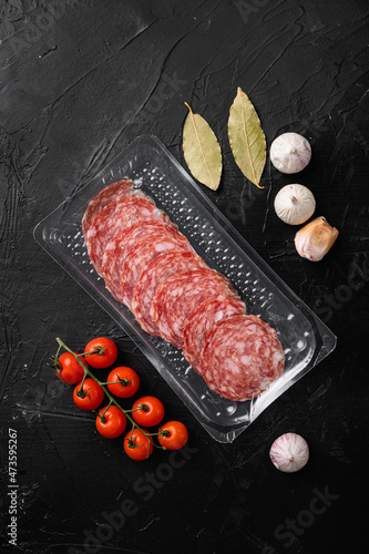 Slices of sausage salami in vacuum package, on black dark stone table background, top view flat lay photo