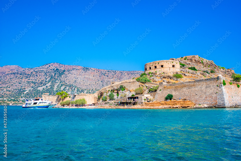 View of the island of Spinalonga with calm sea. Here were isolated lepers, humans with the Hansen's desease, gulf of Elounda, Crete, Greece. View of the island of Spinalonga with calm sea. Here were isolated lepers, humans with the Hansen's desease, gulf of Elounda, Crete, Greece.