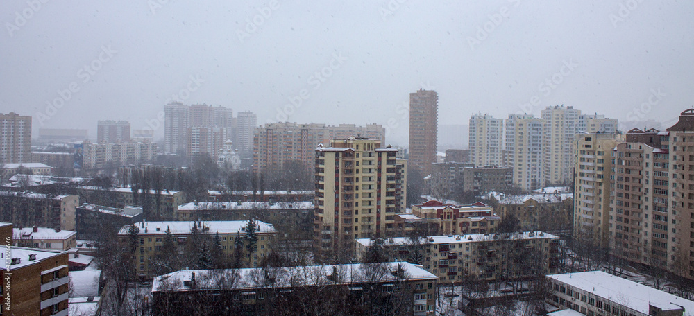 Panoramic top view of a city street with modern multi-storey buildings and snow-covered roofs on a cloudy winter day and space for copying. Concept - urban landscape