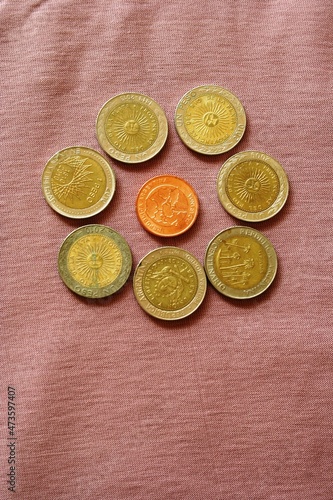 Monedas de metal de curso legal doradas y en cobre,  forman un cìrculo que se parece una flor, con diseño ilustrado con fondo rosa