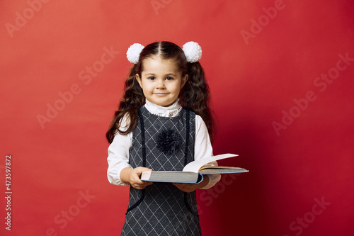 Portrait of a little girl in school uniform looking at camera and holding an open book.