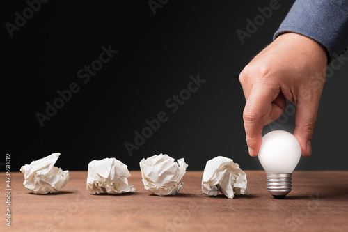 Hand put a glowing light bulb behind the row of crushed paper balls, the problems are the guideline to success, turn mistakes into power, motivation, and achievement concept