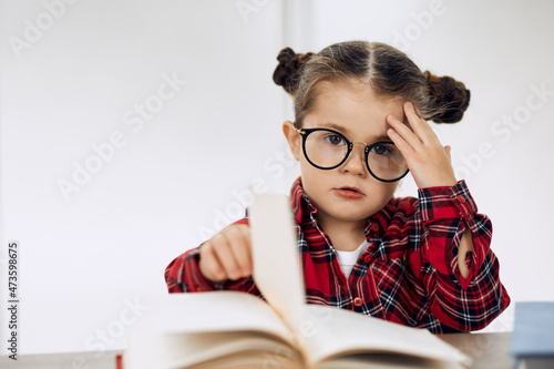 Little girl wearing glasses and doing homework. Turning page.