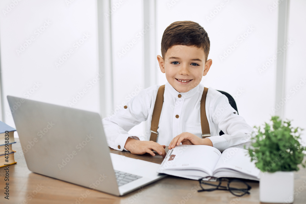 Happy kid doing homework at his work space with a laptop and books. Happy kid doing homework at his work space with a laptop and books.