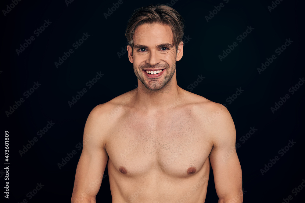 Fototapeta premium Handsome young smiling man isolated. Portrait of shirtless muscular man is standing on black background.