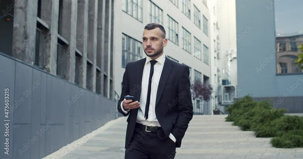 Close up portrait of serious caucasian male professional walking in city and using smartphone. Handsome man manager with cellphone on street outdoors. Businessman concept Close up portrait of serious caucasian male professional walking in city and using smartphone. Handsome man manager with cellphone on street outdoors. Businessman concept