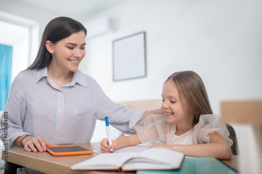 Joyful mother watching her daughter doing homework Joyful mother watching her daughter doing homework