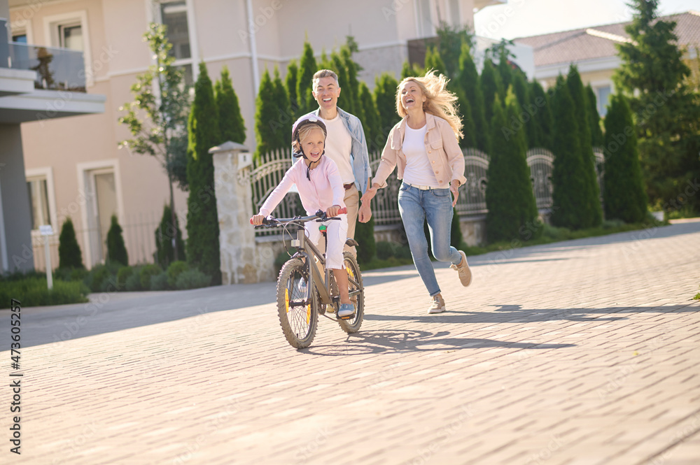 A cute blonde girl learning to ride a bike with her parents
