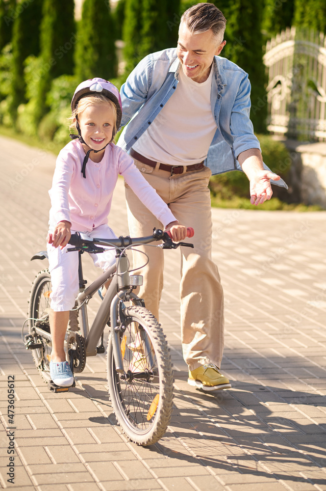 A man supporting a girl while she riding a bike