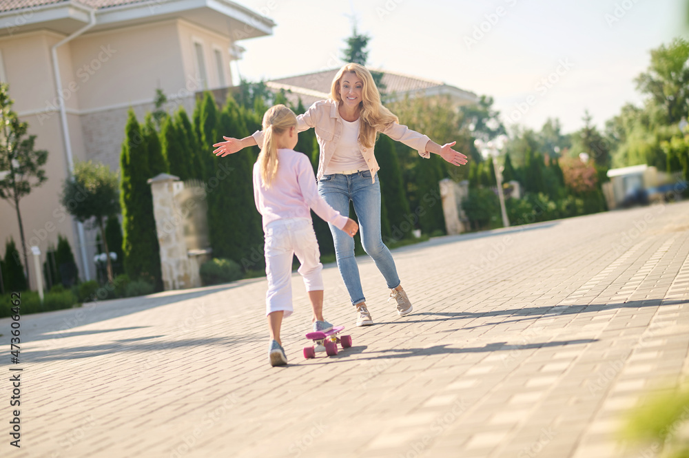 A blonde girl trying skateboarding and feeling excited