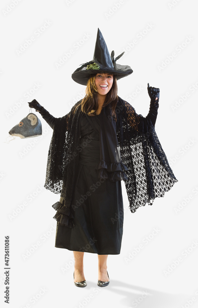 Full length shot of a Hispanic woman dressed as a witch for Halloween holding a mouse head trick or treat bucket dancing, against a white background Full length shot of a Hispanic woman dressed as a witch for Halloween holding a mouse head trick or treat bucket dancing, against a white background