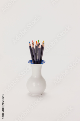 Still life of colored pencils sitting in vase on white background. 