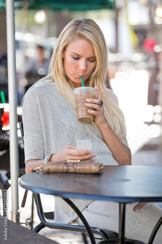 Young woman sitting outside at a cafe on her phone drinking iced coffee. photo