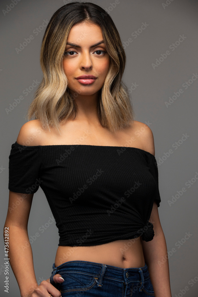 Studio portrait of a young confident Hispanic woman with long hair on gray background. Studio portrait of a young confident Hispanic woman with long hair on gray background.