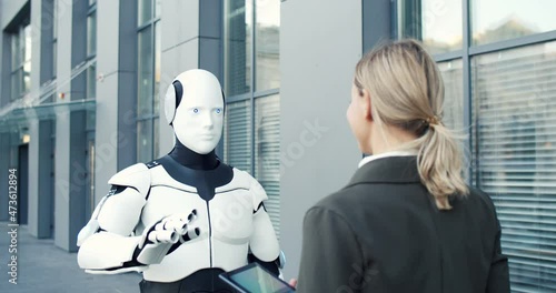 Human-like robot and businesswoman are synchronically moving different parts of their bodies while giving five to each other. Woman managing it with tablet computer photo