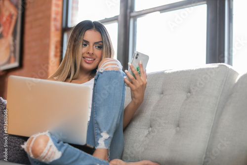 Happy Hispanic woman talking on mobile phone with laptop at home  photo