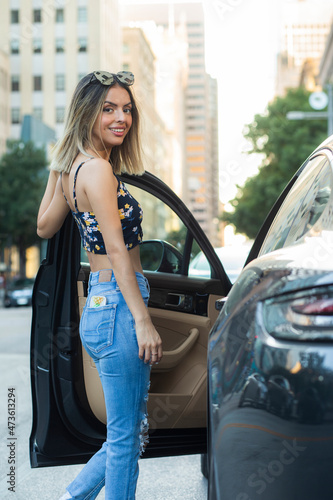 Portrait of Hispanic woman wearing floral top with torn blue jeans, getting into car on busy city street  photo