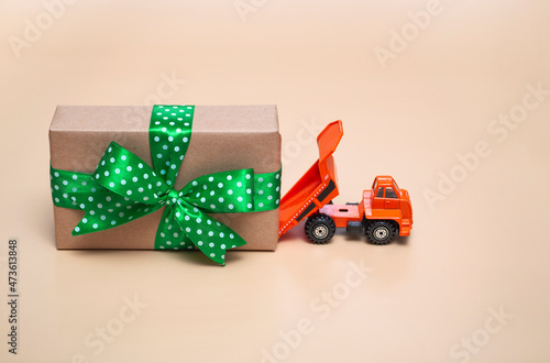 Orange truck with a large gift on a beige background. Holidays concept. With close up, copy space.
