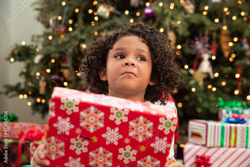 Young girl holding present in front of Christmas tree on Christmas Eve.  photo