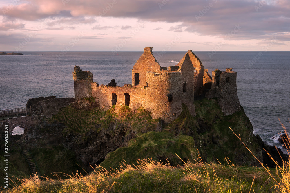 Dunluce Castle Sunset. The iconic ruins of Dunluce Castle perched on a rocky outcrop on the North Antrim Coast in Northern Ireland.