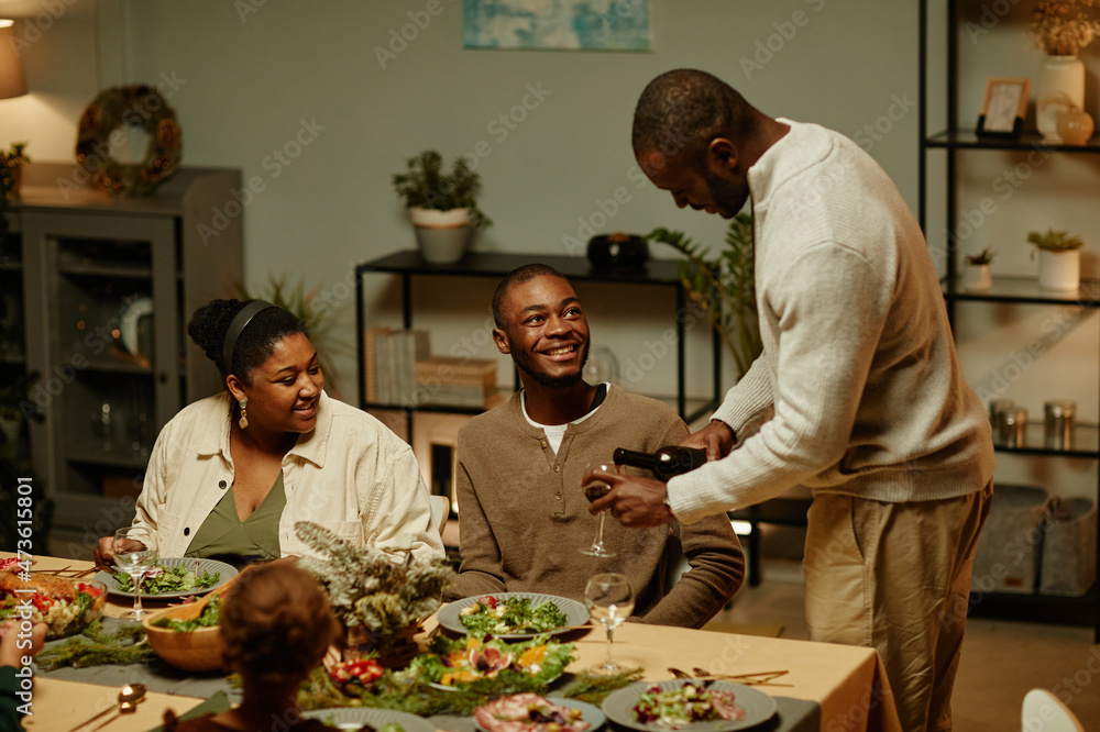 Side view portrait of African-American man pouring wine while enjoying Christmas dinner with family at home Side view portrait of African-American man pouring wine while enjoying Christmas dinner with family at home