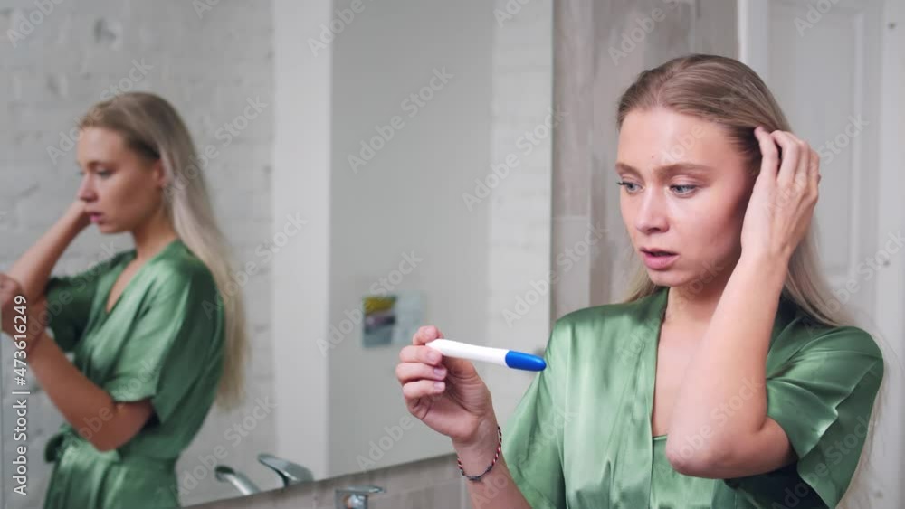Sad young woman holding pregnancy test standing in bathroom. Realtime Sad young woman holding pregnancy test standing in bathroom. Realtime