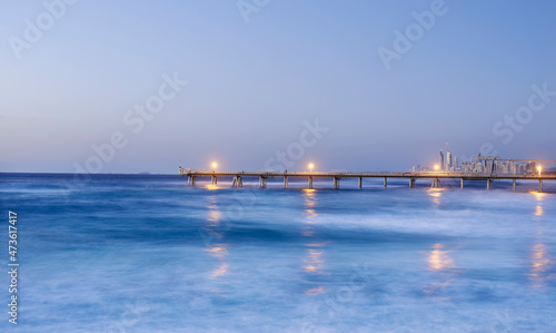 Long pier stretching out into calm ocean in early evening with lights on photo