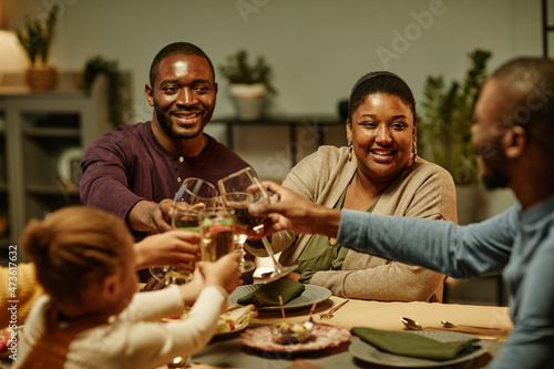 Portrait of happy African-American family clinking glasses while enjoying dinner party at home
