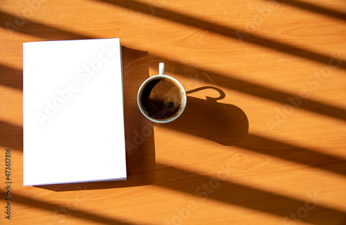 A book and a cup of Turkish coffee on a wooden table with beautiful sunlight