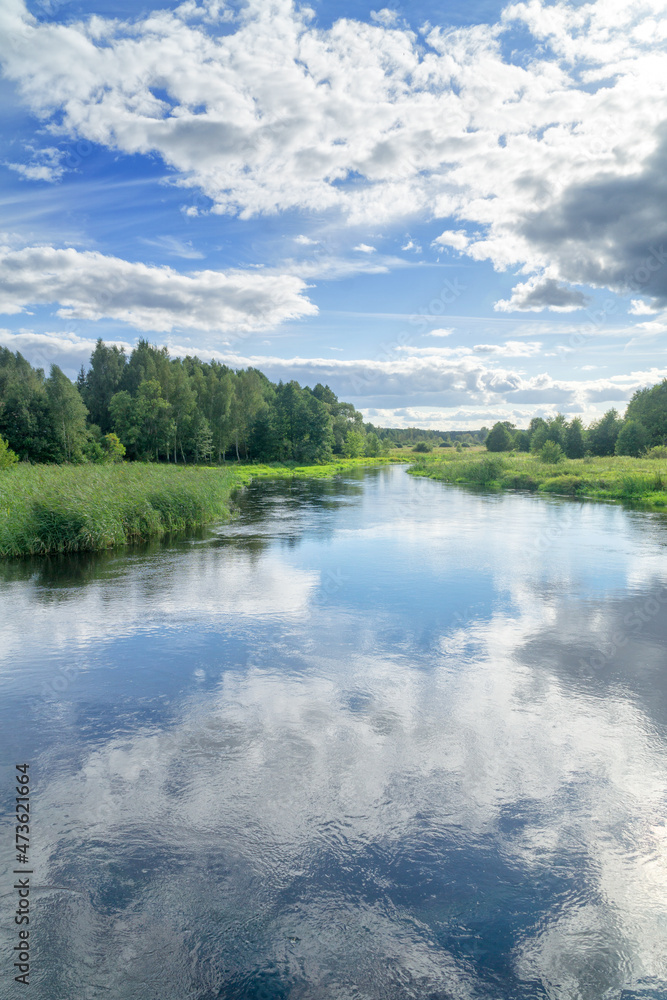 Landscape Suprasl River in Podlasie, Poland. The river flows among meadows and forests, the blue sky with white clouds is reflected in the water. Sunny summer day, nobody. 