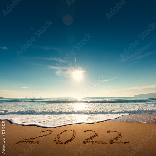 Beautiful sunrise over the sea. Happy New Year 2022 written on seashore.