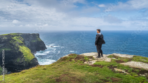 Man standing on the top of iconic Cliffs of Moher and admiring spectacular view, popular tourist attraction, Wild Atlantic Way, County Clare, Ireland photo