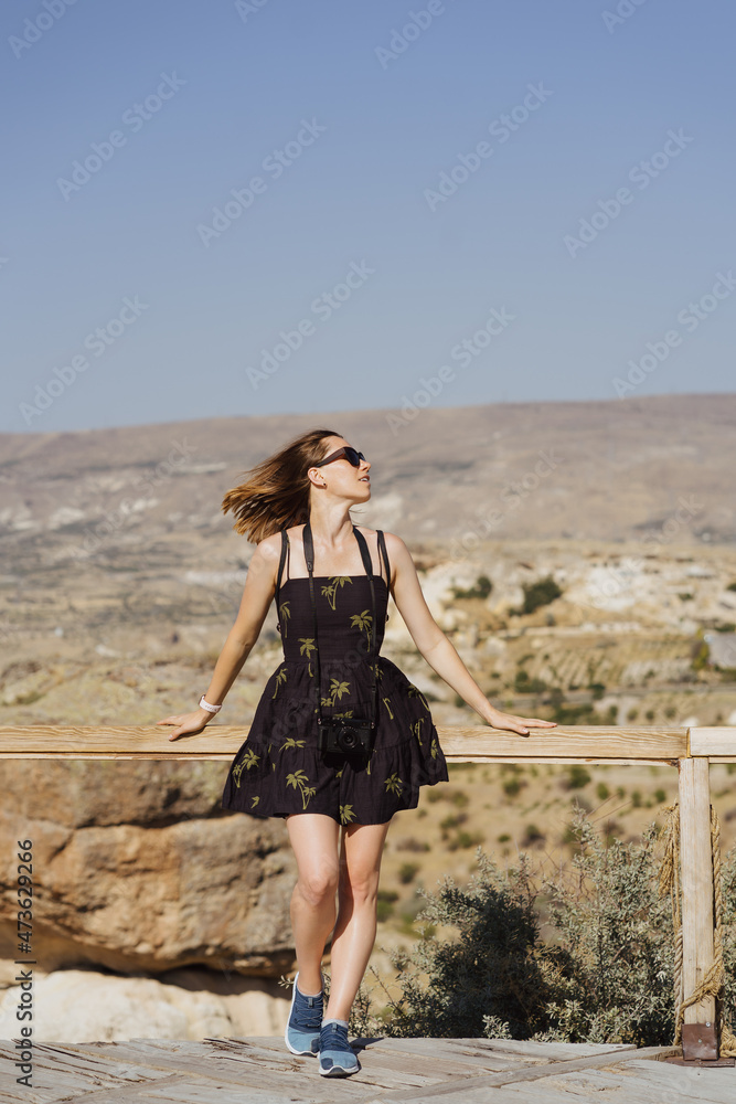 Young woman enjoying beauty of nature looking at mountains in Cappadocia. Adventure travel in Turkey, Europe. Woman stands on a wooden view point on a background with mountain.