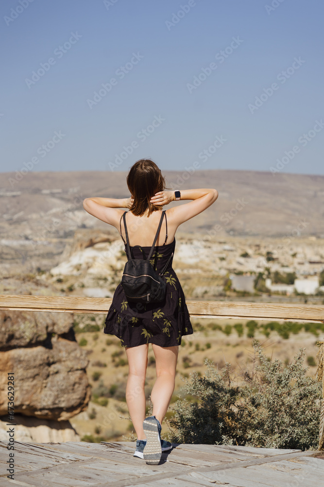 Young woman enjoying beauty of nature looking at mountains in Cappadocia. Adventure travel in Turkey, Europe. Woman stands on a wooden view point on a background with mountain.