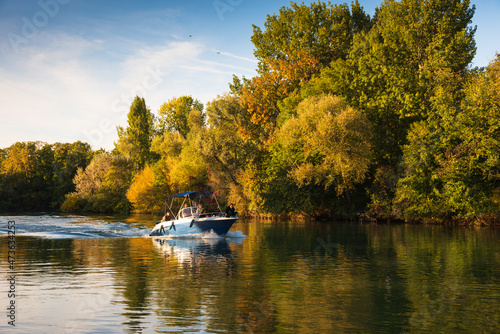 Motorboat with unrecognizable people moving along scenic river in sunny autumn day. Marne river, Ile-de-france, France.