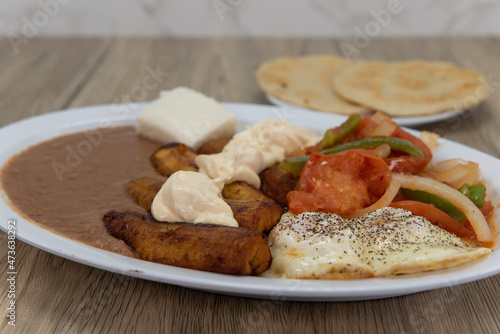Fried plantains on a plate with refried beans, stir fried vegetables, and eggs served sunny side up with pupusa bread for a Latino meal photo