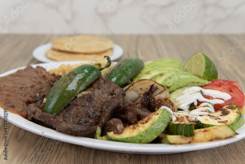 Perfectly grilled steak on a plate with Latino rice and sliced avocados and pupusa on the side