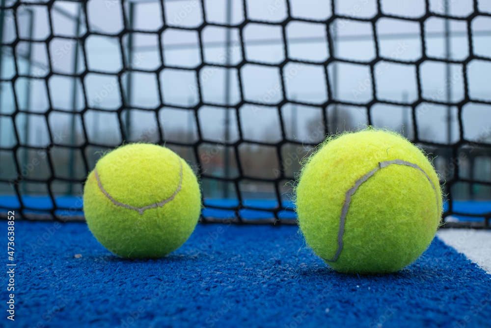 Selective focus. Two paddle tennis balls on a blue court with the net out of focus in the background
