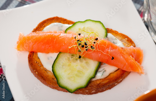 Slices of salmon and cucumber served on toasted baguette with cream sauce on white plate