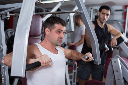 Muscular man doing strength training on fitness machine in modern gym