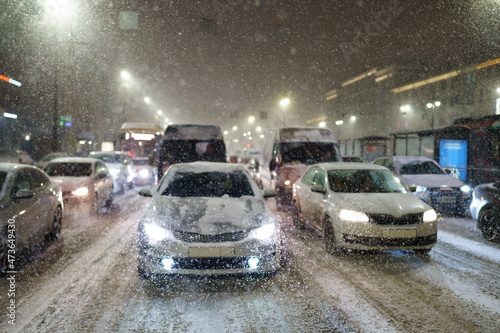 Snowfall and blizzard in city. Cars standing in traffic jam on road due to snow storm, bad visibility, cyclone. Snowstorm cause traffic collapse and vehicles wait for maintenance services till night