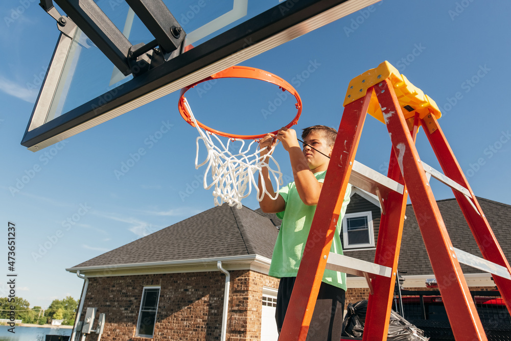 Teenager hanging up new basketball net. Stock Photo Adobe Stock